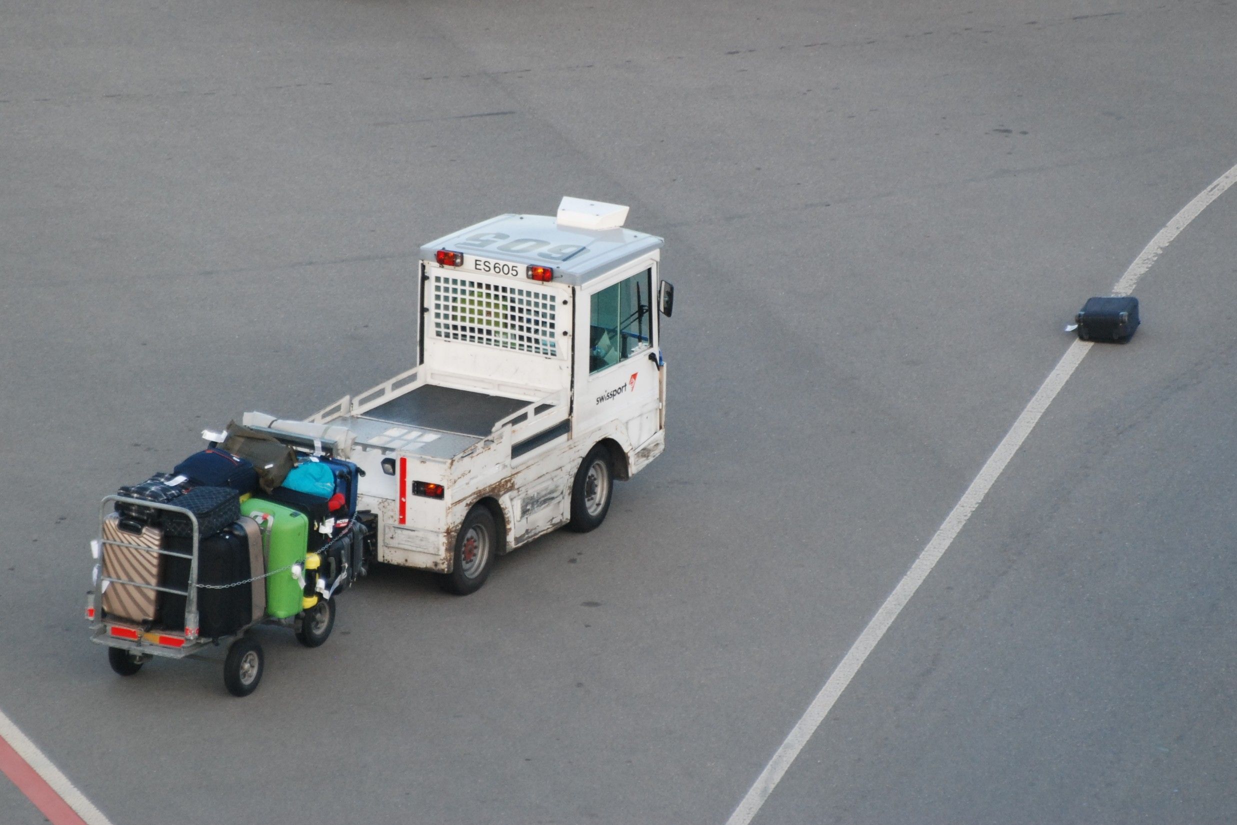 Swissport Gepäckfahrzeug auf Rollfeld; ein einzelner schwarzer Koffer sichtbar von anderem Gepäck getrennt.
