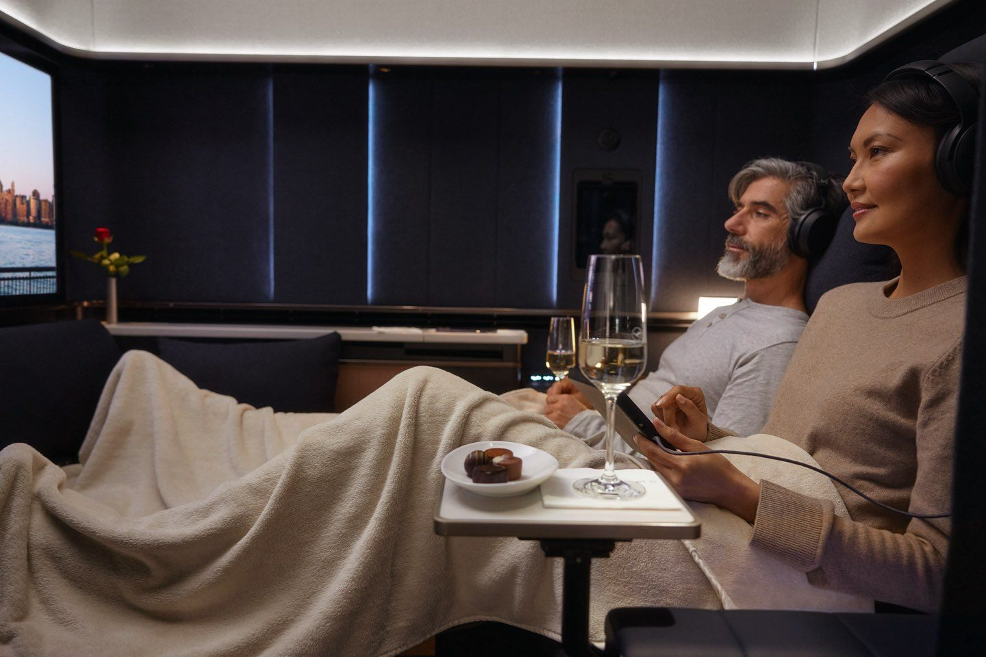 Two passengers elbow-to-elbow in Lufthansa's first class suite, with a wine glass precariously balanced on a narrow side table