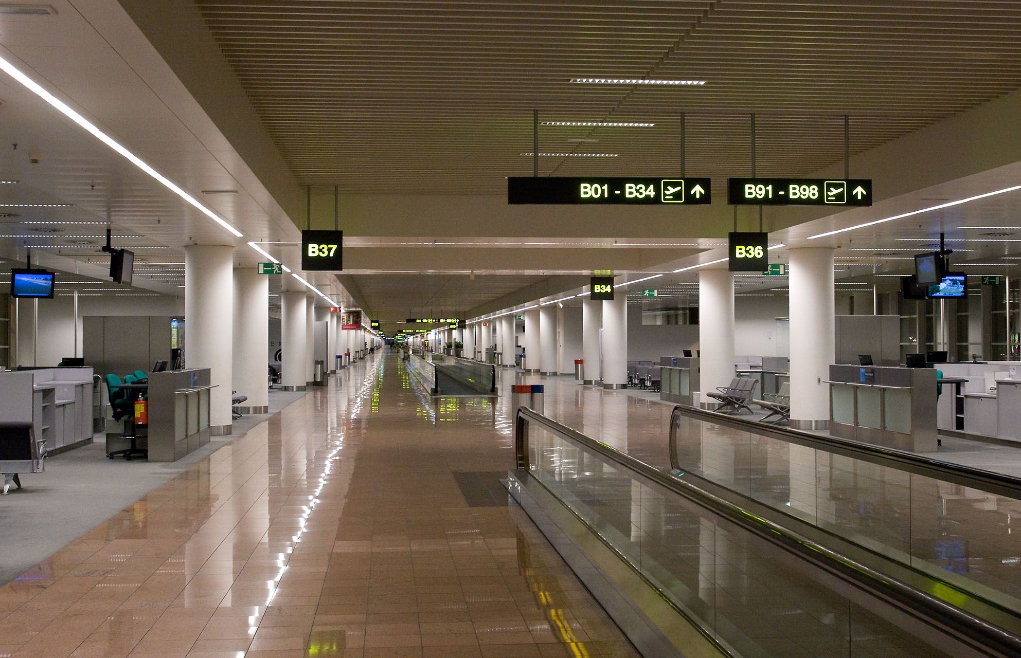Empty airport terminal hallway with moving walkway and gate signs.