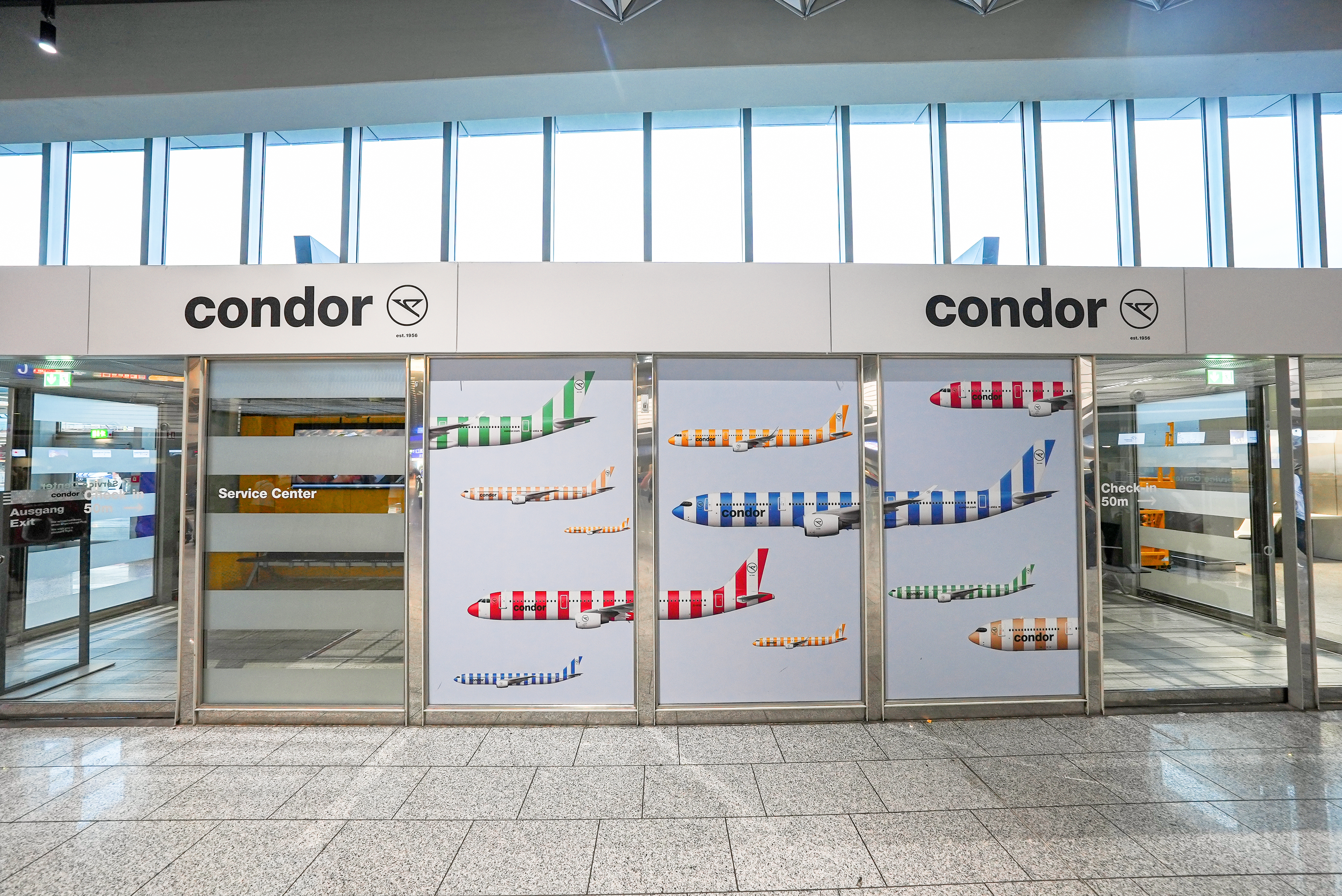 Condor-Werbung am Frankfurter Flughafen mit Flugzeugen in farbigen Streifenlackierungen.