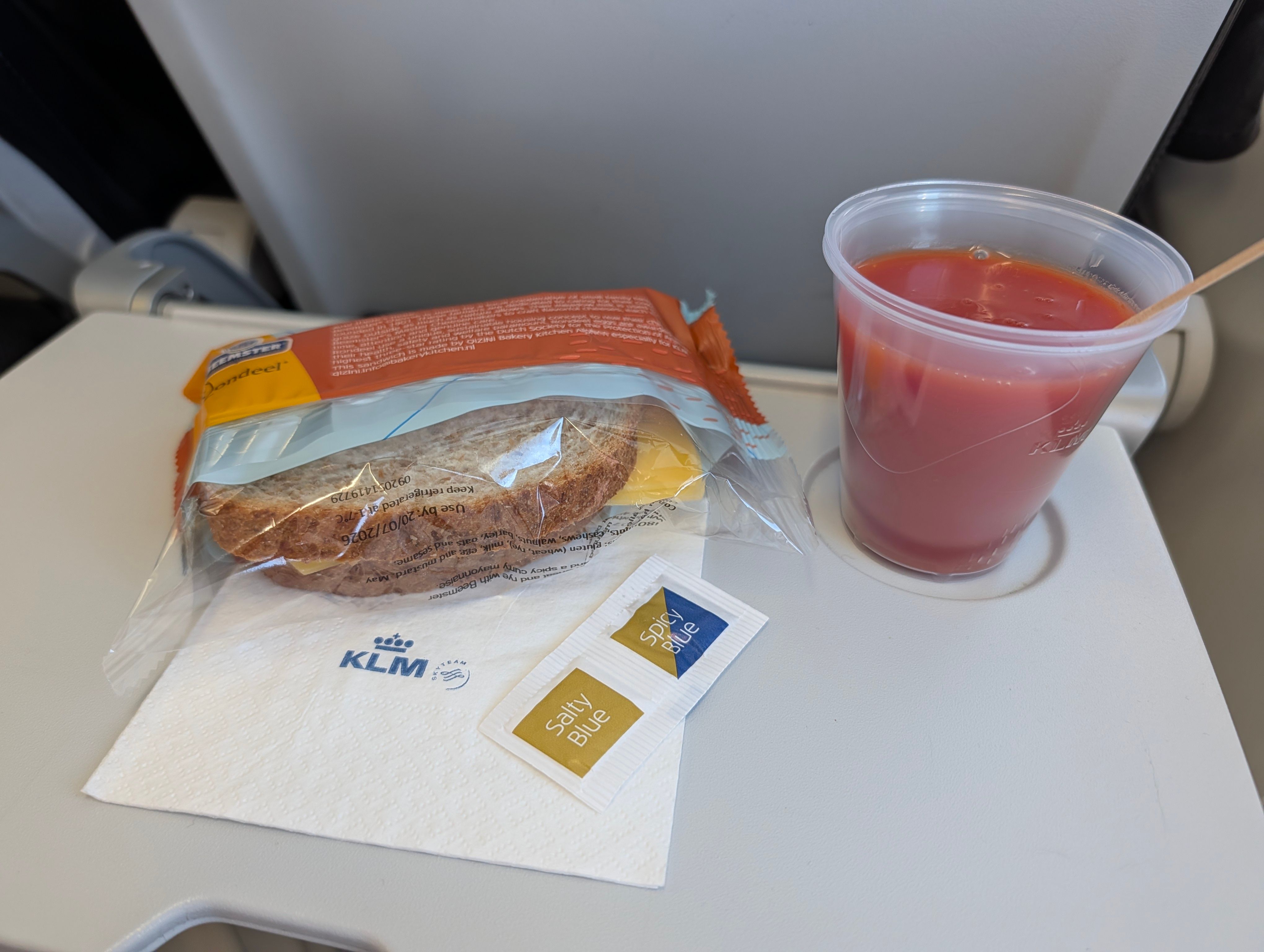 Ein verpacktes Sandwich, Tomatensaft, KLM-Serviette und Gewürze auf einem Flugzeug-Serviertablett als Bordmahlzeit.