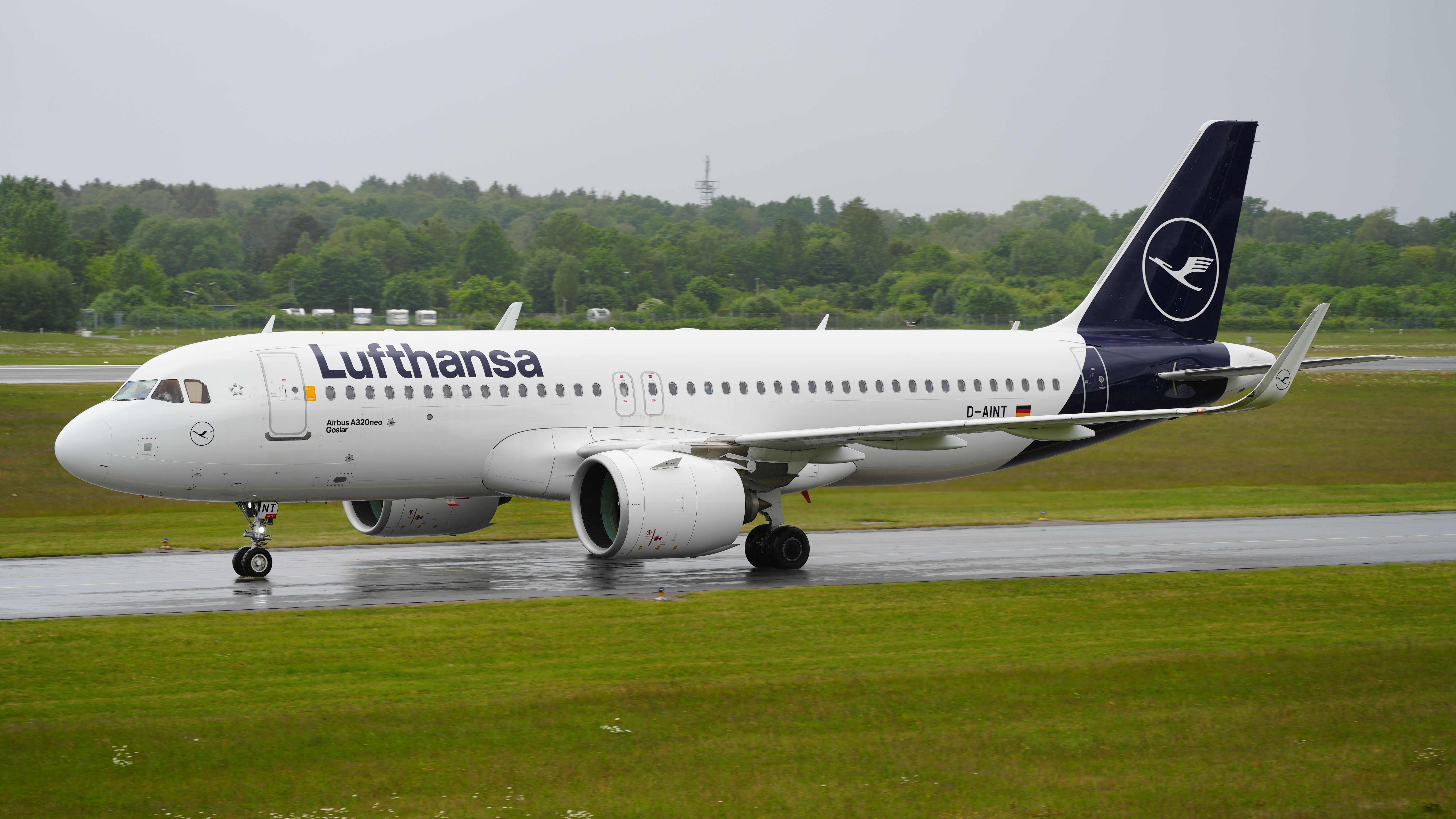 Lufthansa A320neo taxis on a rainy runway. Visibility is low.