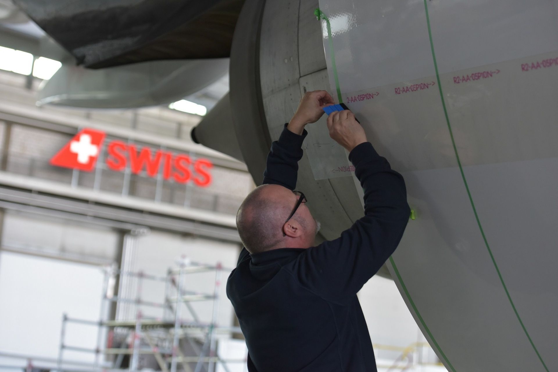 Ein Techniker bringt Folie an einem SWISS Flugzeug im Hangar an.