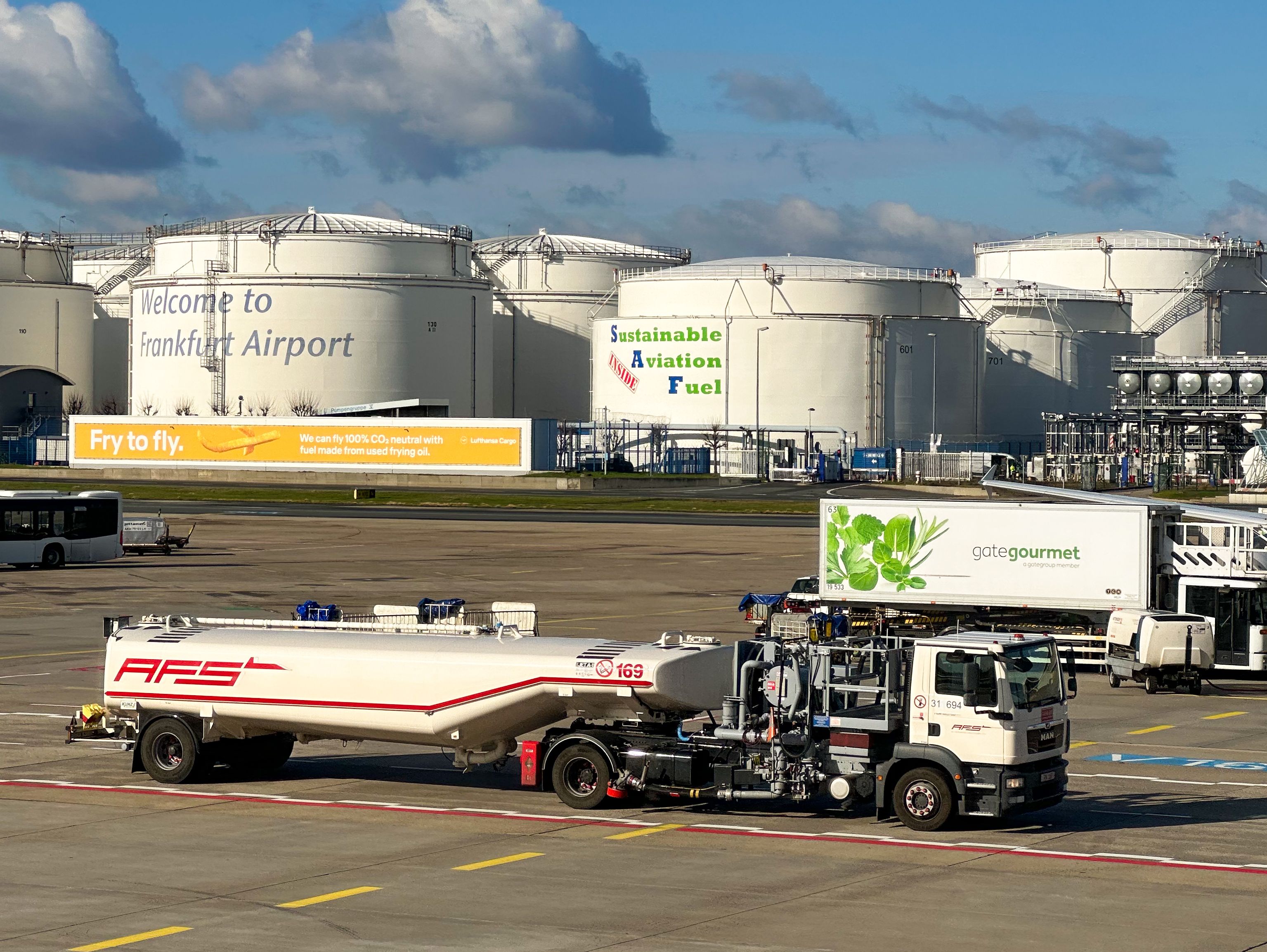 Fuel truck at Frankfurt Airport with sustainable aviation fuel ads on nearby storage tanks.