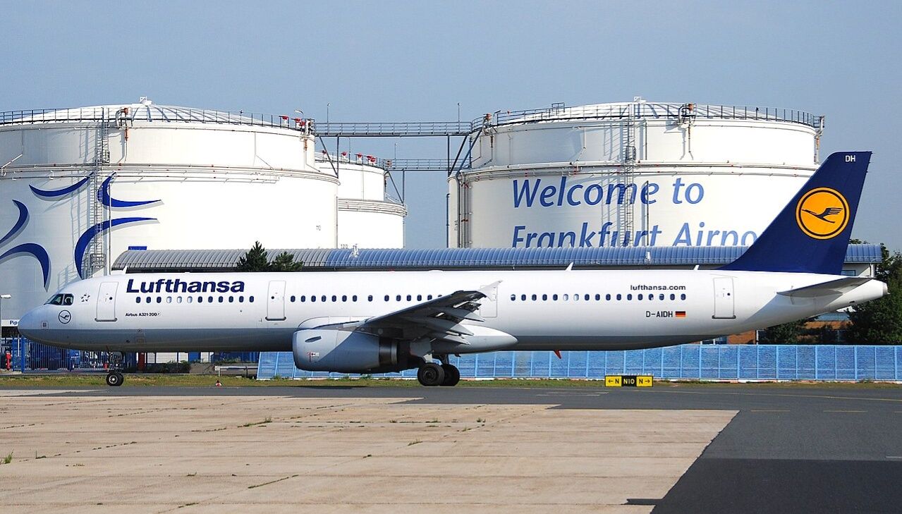 A Lufthansa aircraft taxis past large fuel storage tanks at Frankfurt Airport