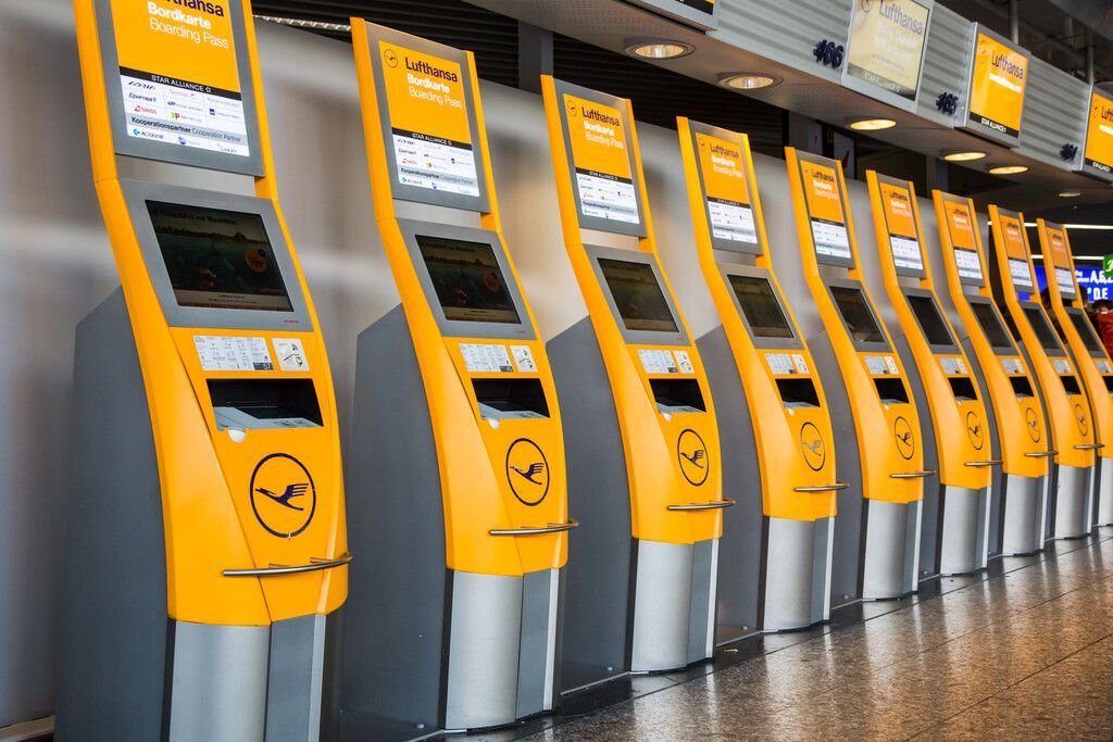A row of yellow Lufthansa self-service check-in kiosks at an airport terminal.