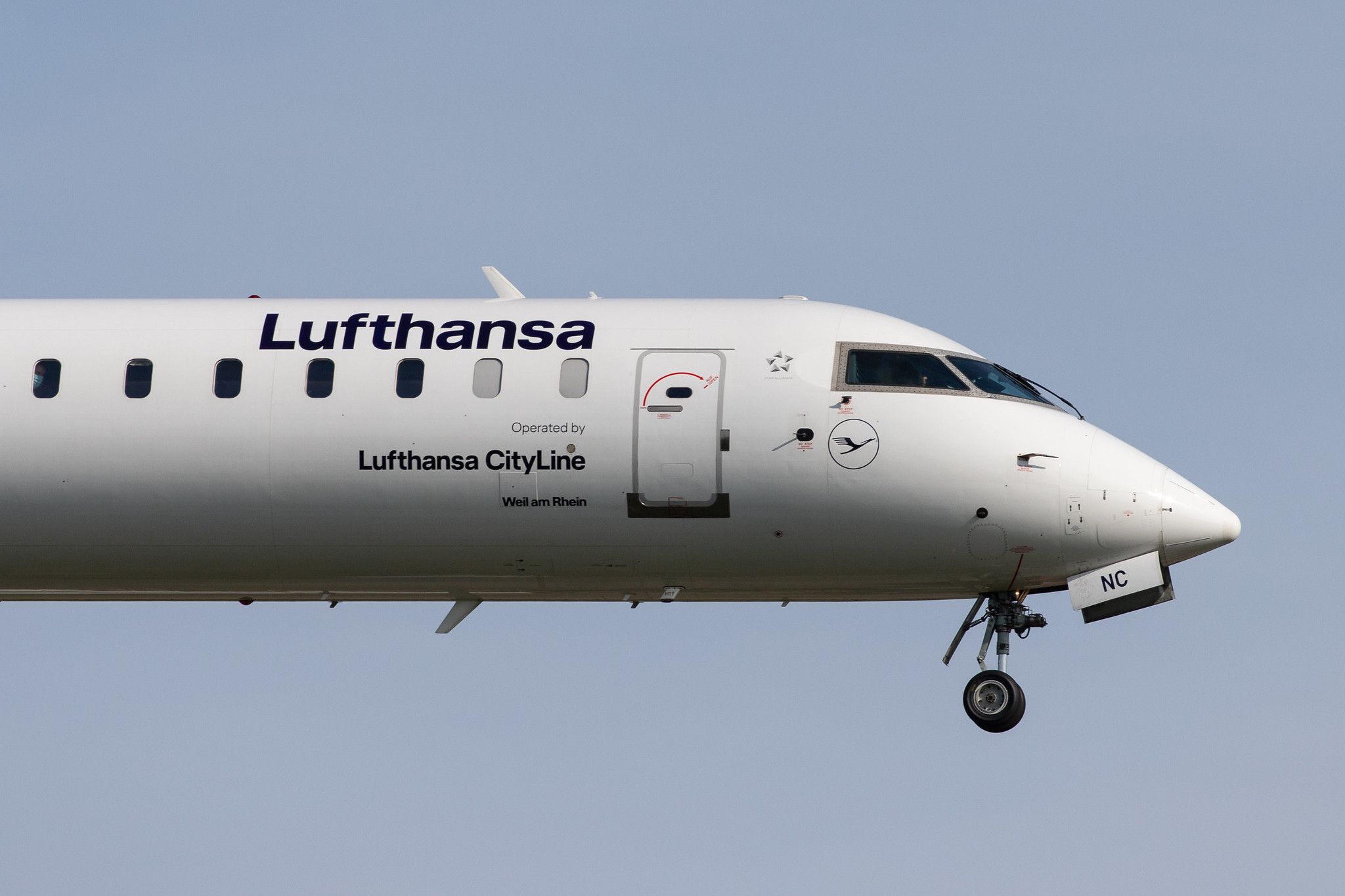 Nahaufnahme einer Lufthansa CityLine Bombardier CRJ-900 im Flug vor klarem blauen Himmel.
