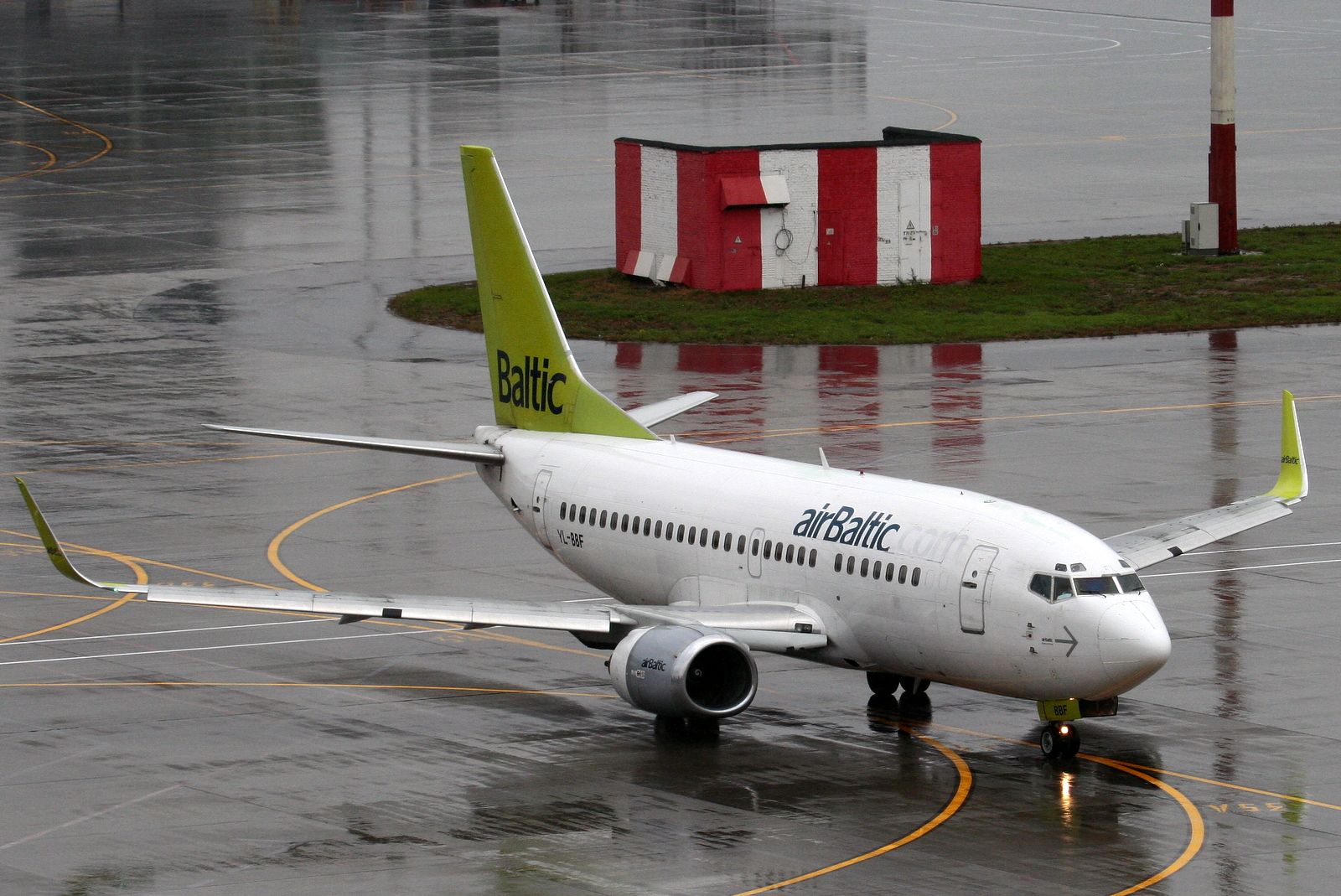 YL-BBF airBaltic B737-500 auf nassem Rollfeld am Flughafen Sheremetyevo mit rot-weißem Gebäude.
