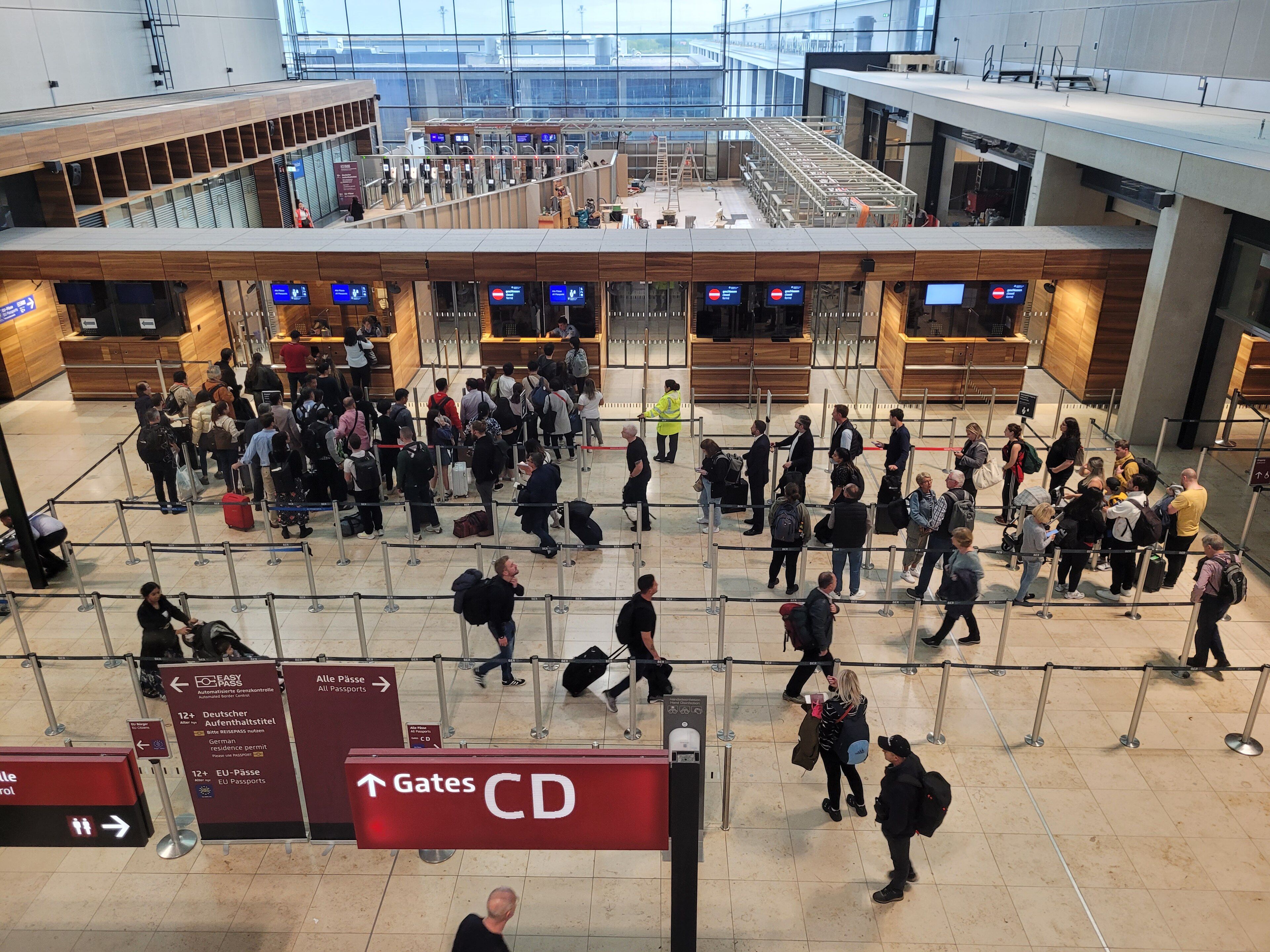 Crowded passport control at BER Airport; travelers waiting in line.