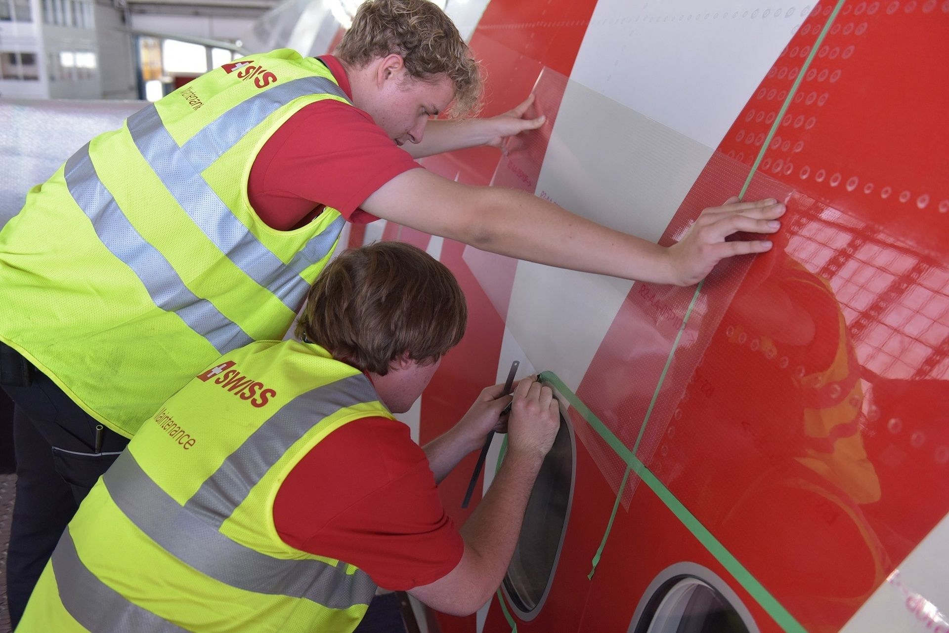 Zwei Mitarbeiter von SWISS Maintenance tragen AeroSHARK sorgfältig auf einen Flugzeugrumpf auf.