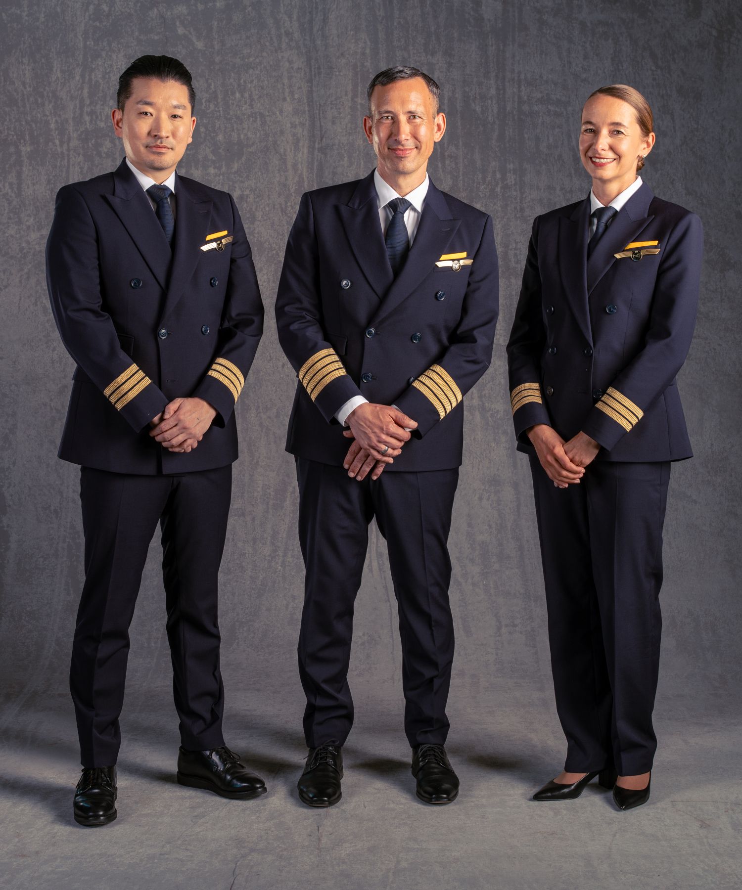 Three Lufthansa pilots stand together in formal BOSS-designed uniforms against a neutral grey background.